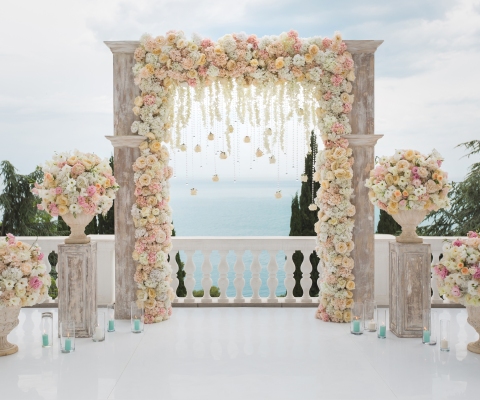 Elegant wedding arch with fresh flowers, vases on background of ocean and blue sky.